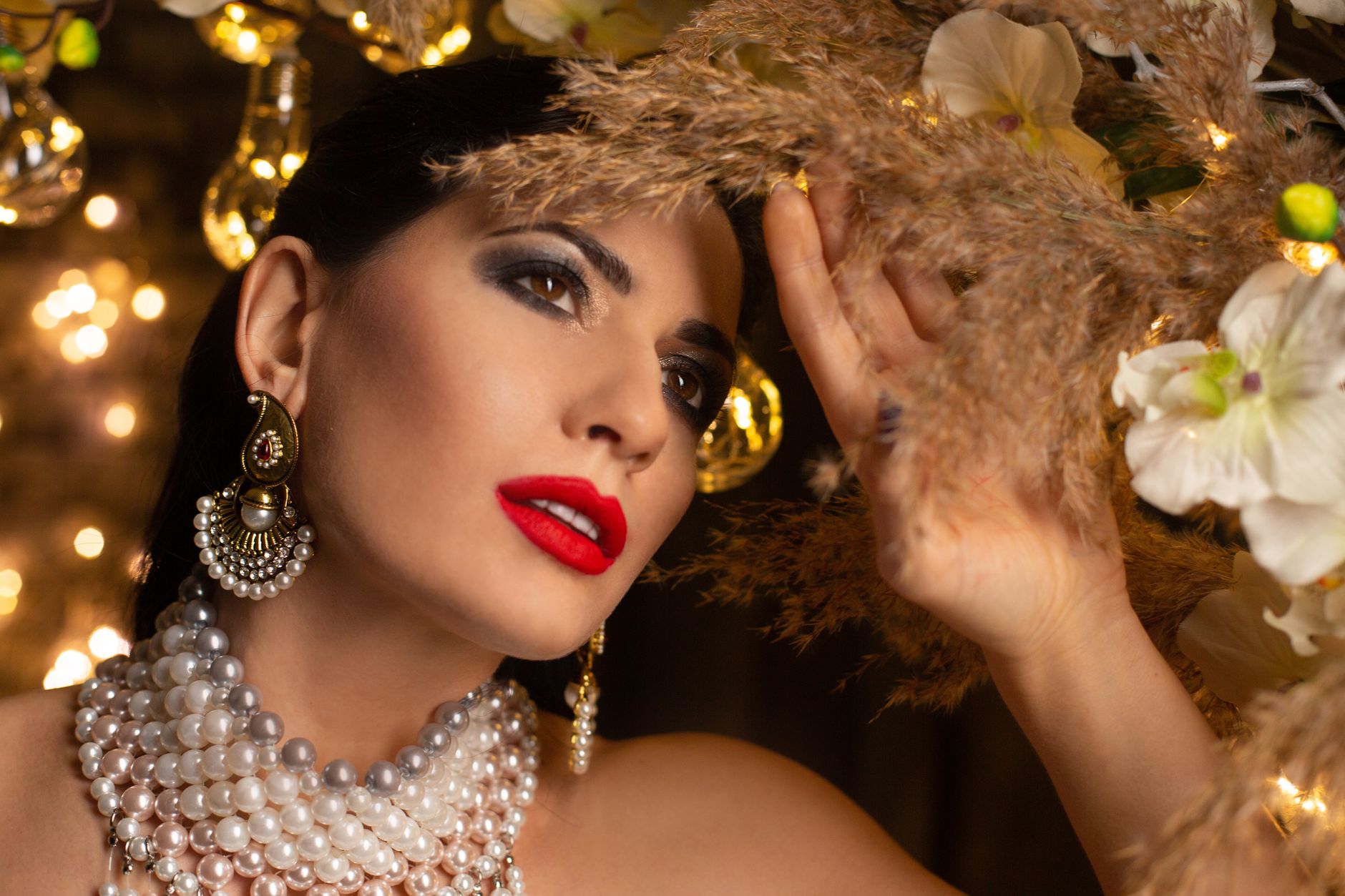 Stylish lady with bright makeup in expensive pearl necklace and earrings standing in room with festive decorations and golden
